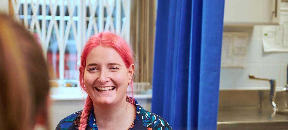 Woman with pink hair smiling with someone  enthusiastically